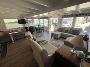 Een ruime woonkamer met een zithoek, een salontafel en een televisie. Er is een eethoek met een tafel en stoelen.