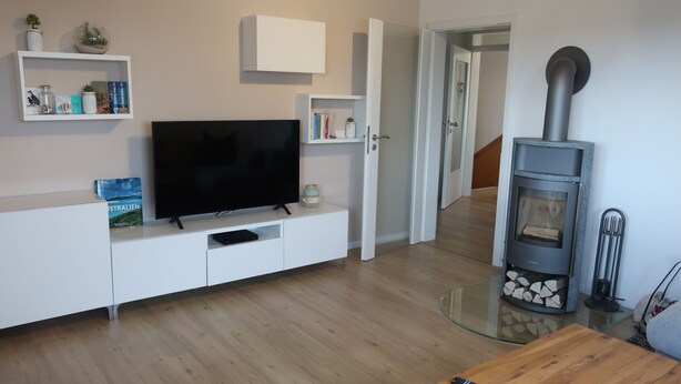 A modern living room with a flat-screen TV, white cabinetry, a glass coffee table, and a wood-burning stove.
