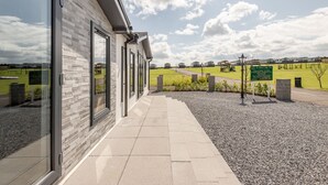A modern building with large windows and a paved walkway leading to a grassy area with a signboard. - Lodge No 10 | St Andrews Lodge Park (Strathkinness)