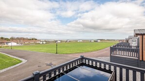 A view of a residential area with a paved driveway, a grassy field, and a row of houses. - Lodge No 10 | St Andrews Lodge Park (Strathkinness)