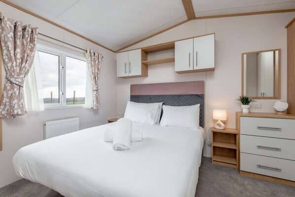 A neatly arranged bedroom with a bed, bedside tables, a dresser, and a window with curtains.