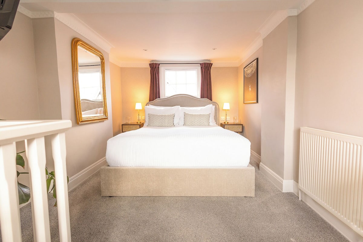 A neatly arranged bedroom with a large bed, bedside lamps, a mirror, and a radiator.