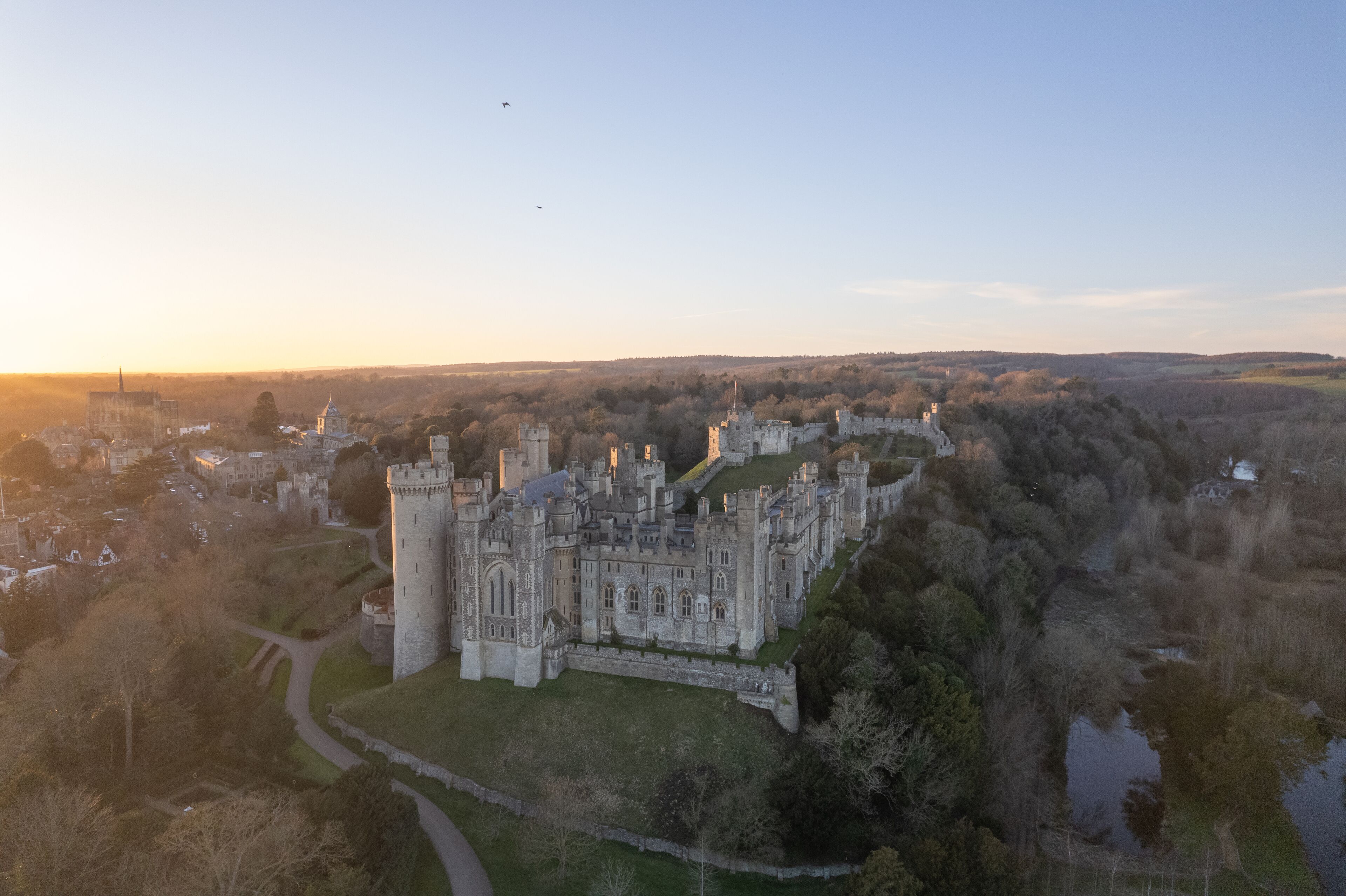 An aerial view of a historic castle with a moat, surrounded by trees and a clear sky.
