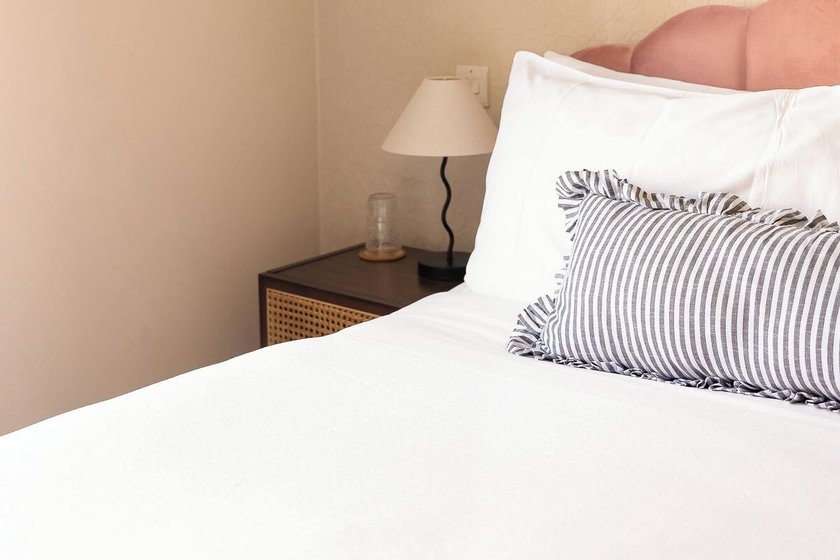 A neatly made bed with striped pillows, a bedside lamp, and a framed artwork on the wall.