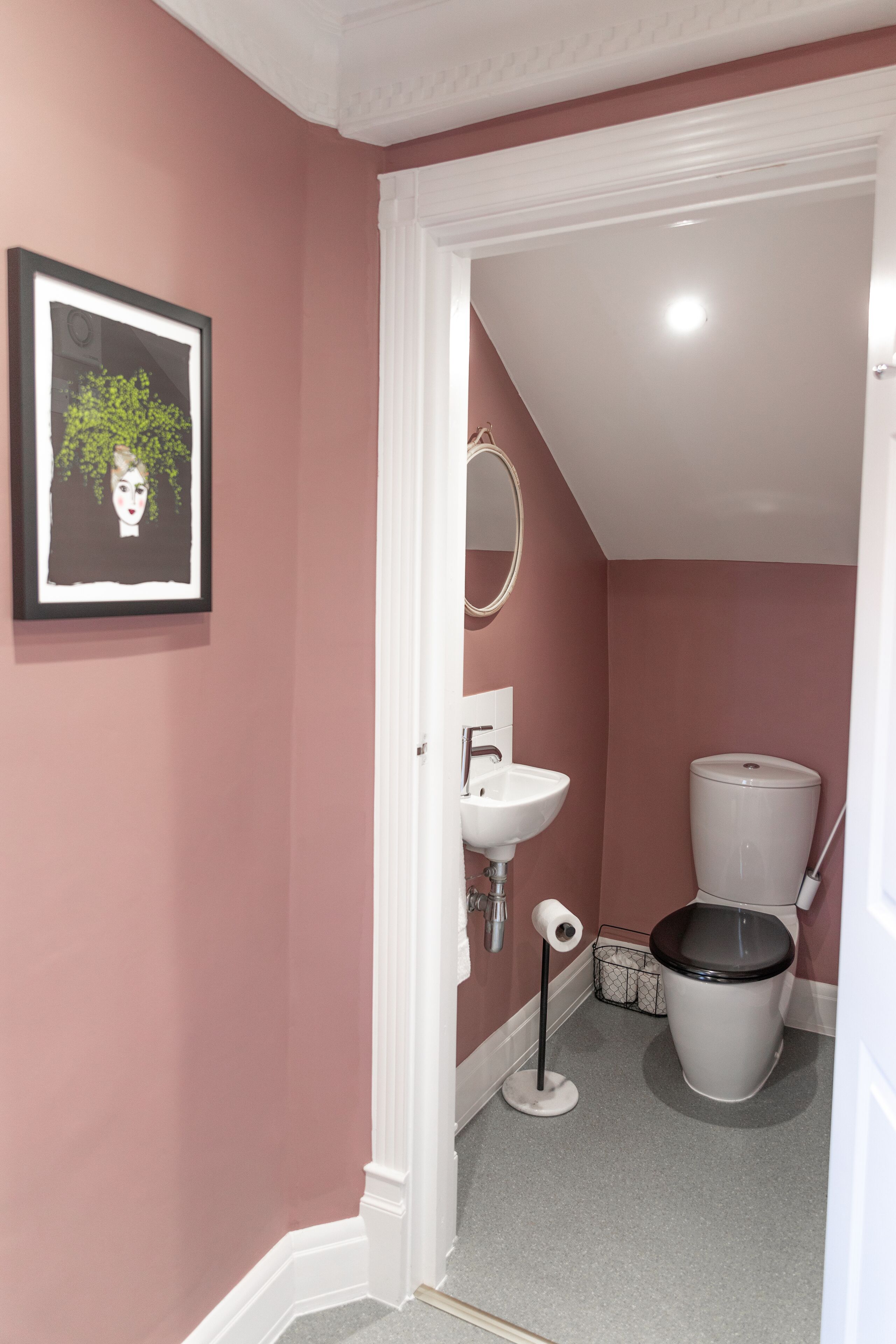 Un baño con paredes rosas, un lavamanos blanco, un inodoro y un cuadro en la pared.