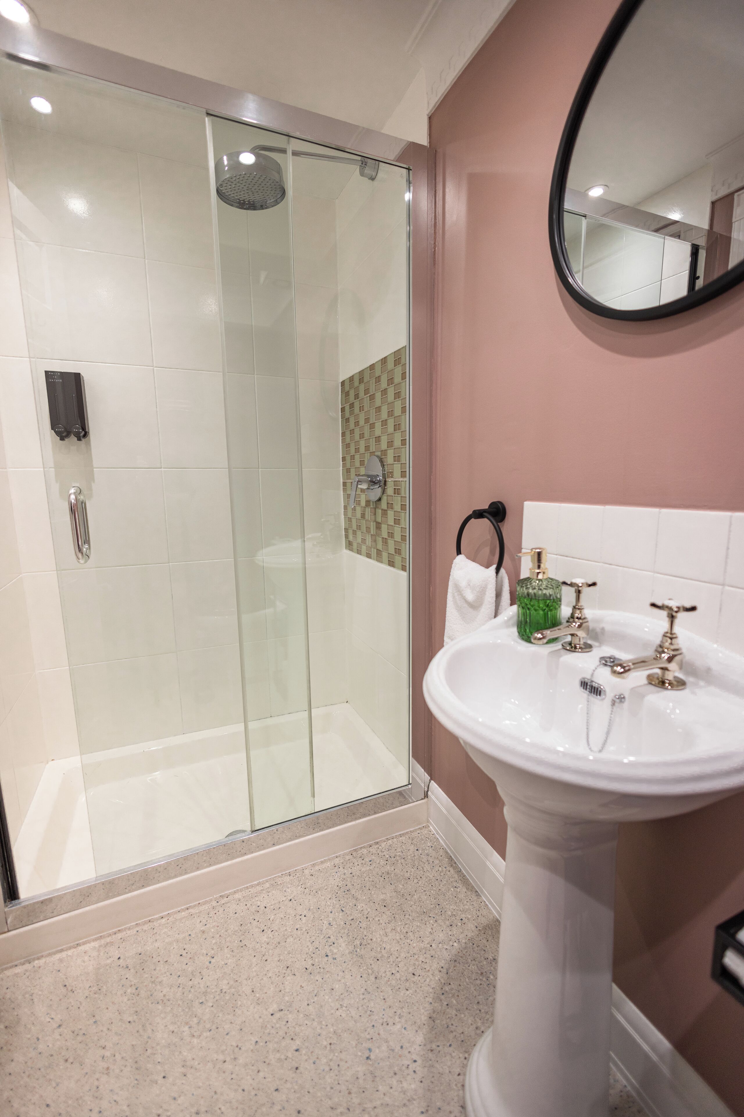 A bathroom with a glass-enclosed shower, a white pedestal sink, and a mirror on the wall.
