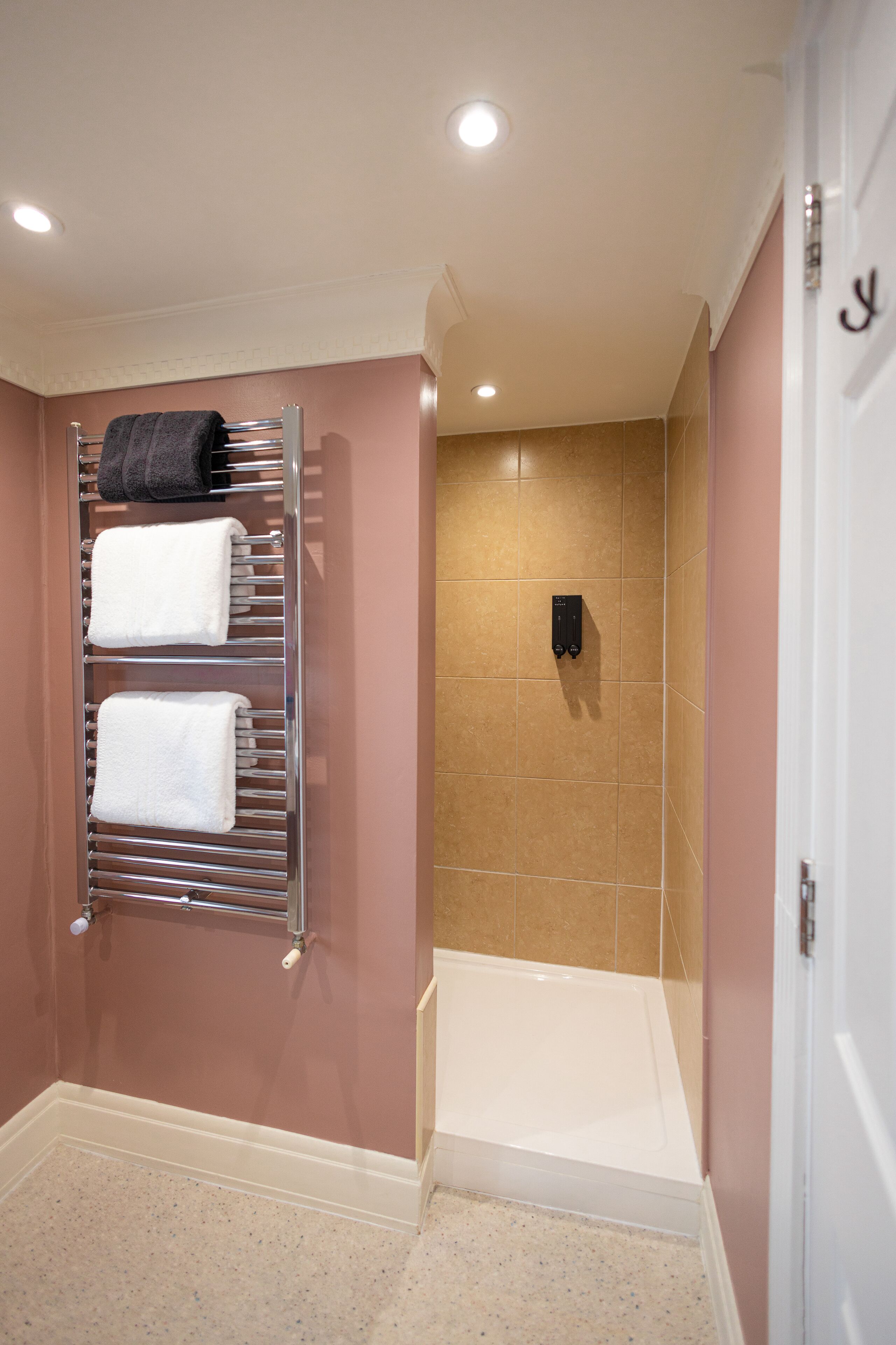 Un baño con un perchero que sostiene dos toallas, una zona de ducha con azulejos color beige y una bañera blanca.