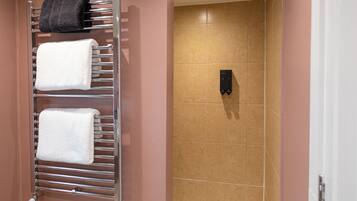 Un baño con un perchero que sostiene dos toallas, una zona de ducha con azulejos color beige y una bañera blanca.