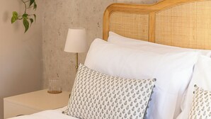 Cama bem arrumada com almofadas estampadas, luminária de cabeceira e planta pendente.