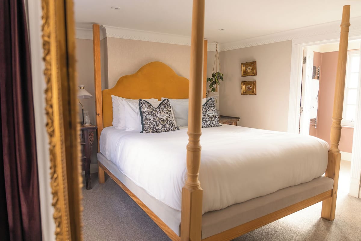 A four-poster bed with white linens, a wooden headboard, and patterned pillows.