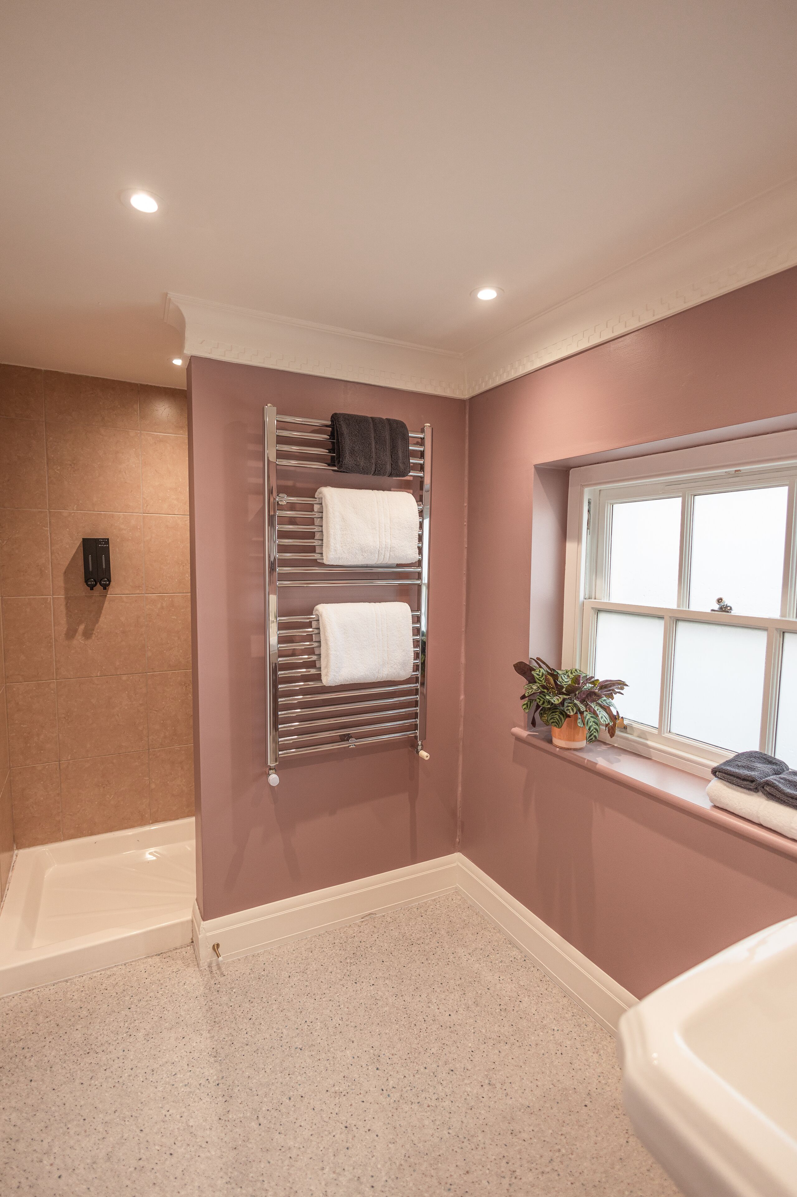 A bathroom with a bathtub, a towel rack with towels, a potted plant, and a window.