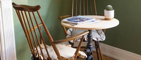 A dining area with a round table, two wooden chairs, a small potted plant, and a wall-mounted lamp.