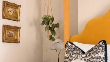 Een slaapkamer met een bed, een hangplant, twee ingelijste foto’s en een nachtkastje met een lamp.