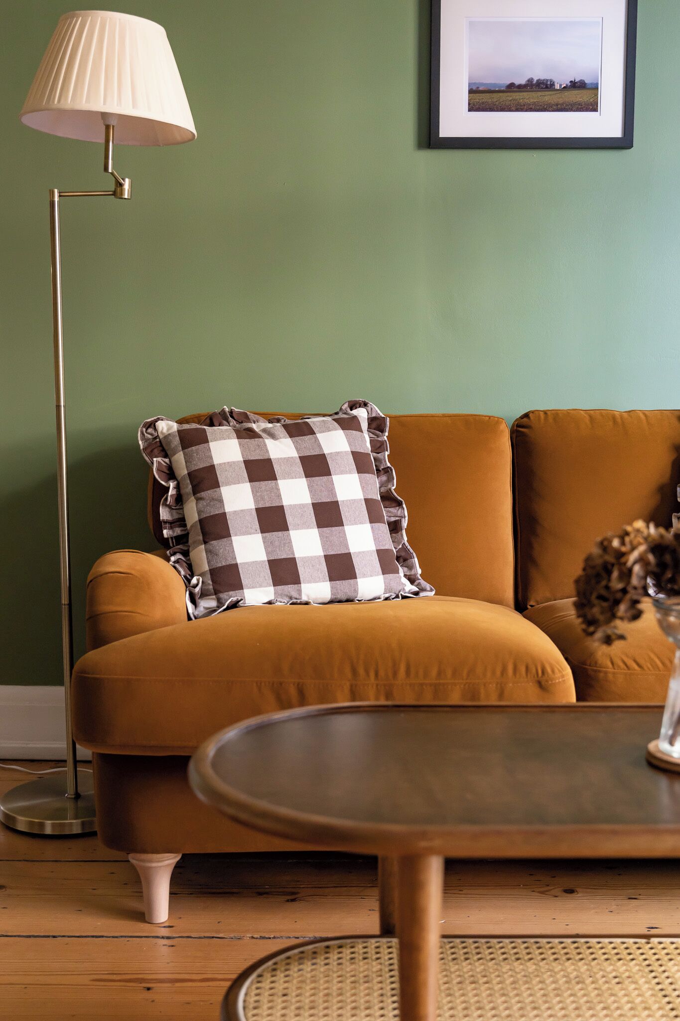 A sofa with a checkered pillow, a floor lamp, and a framed picture on a wall.