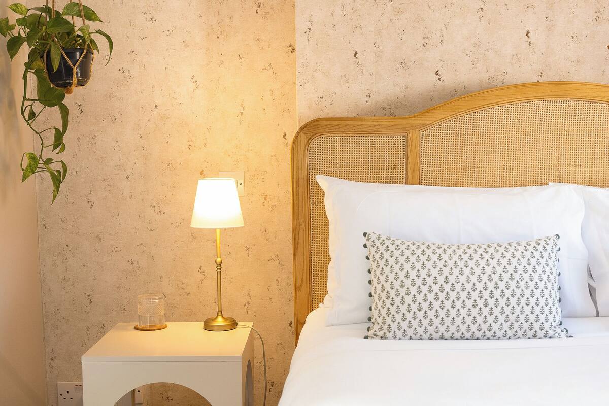 A neatly made bed with a woven headboard, a bedside lamp, and a potted plant.