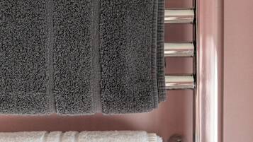 A metallic towel rack with two towels, one dark and one white, against a pink wall.