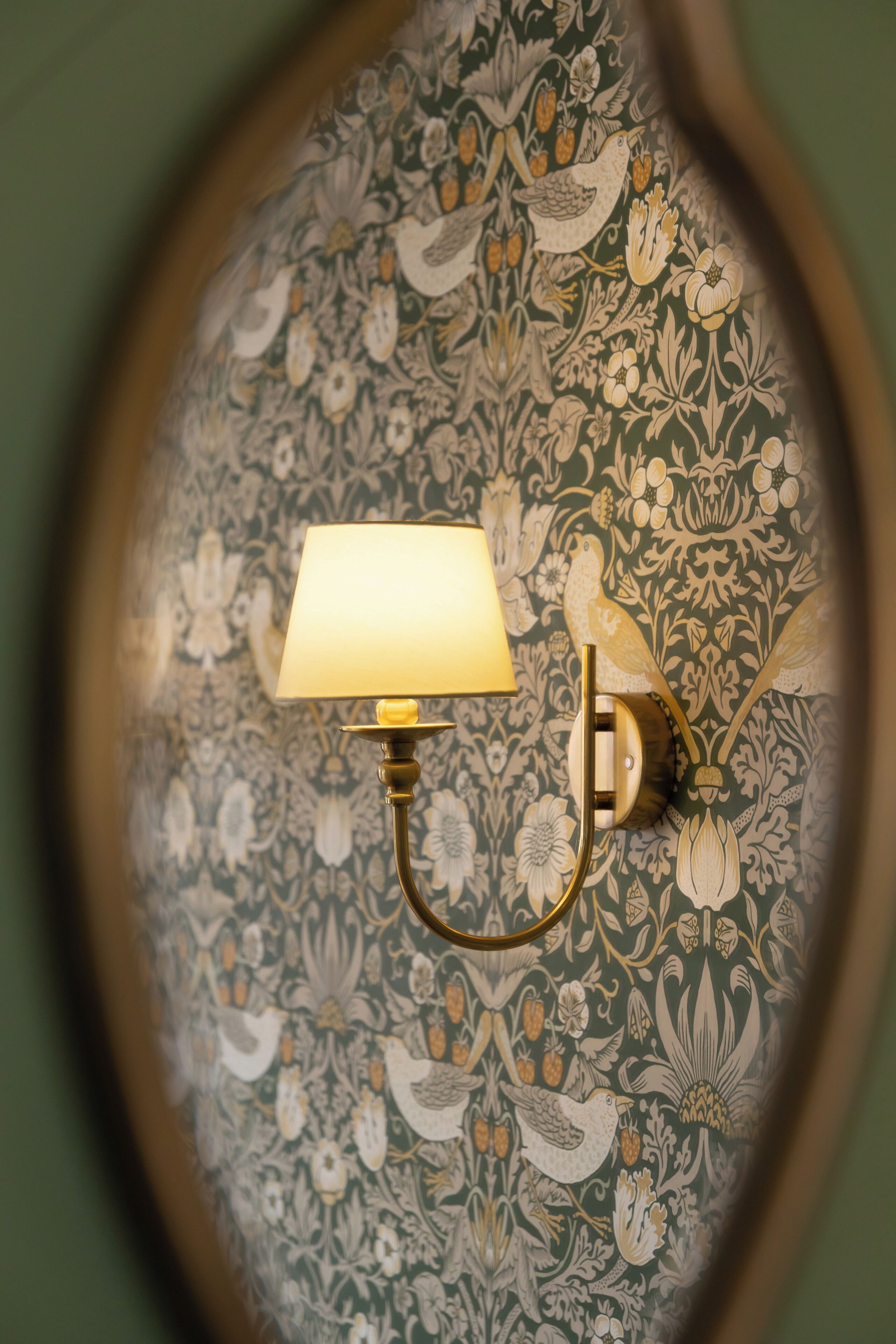 A wall-mounted lamp with a light on a floral wallpaper.