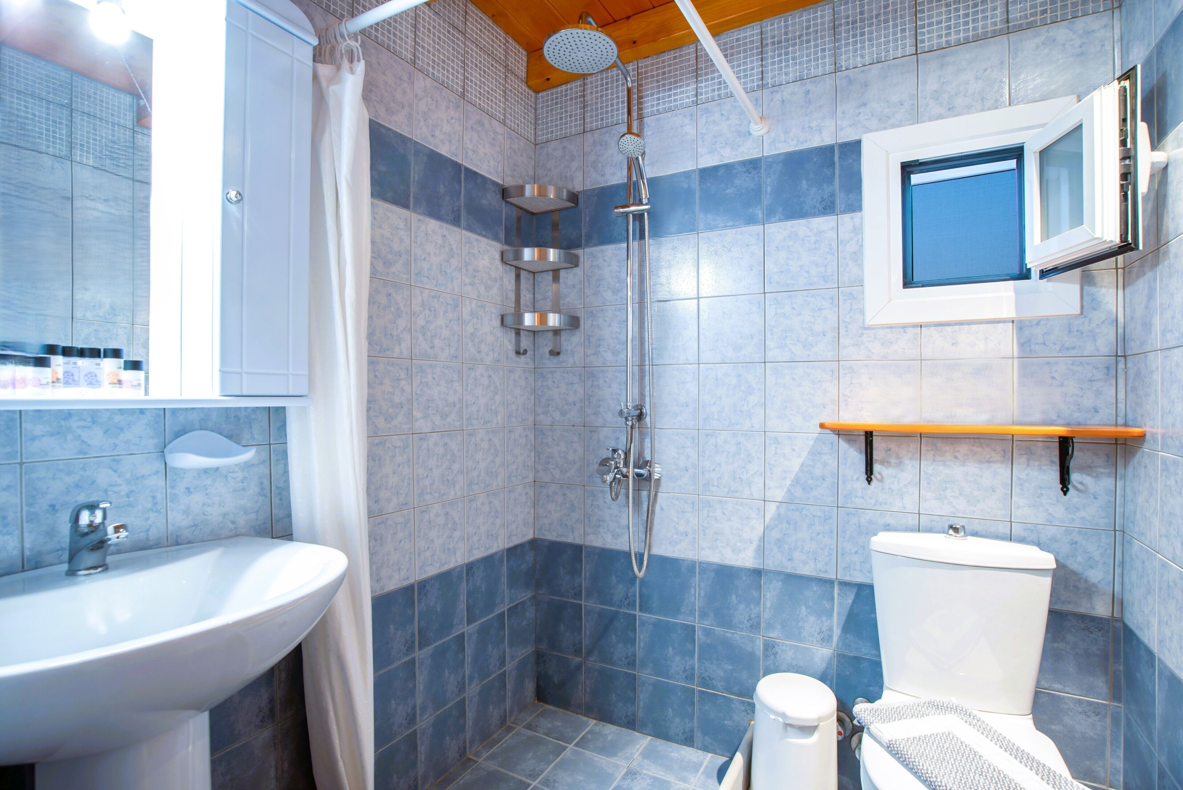 A bathroom with a shower, sink, toilet, and a window.