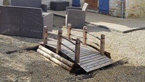 En bygning i sten med en træterrasse, fletningsmøbler og et grusunderlag.