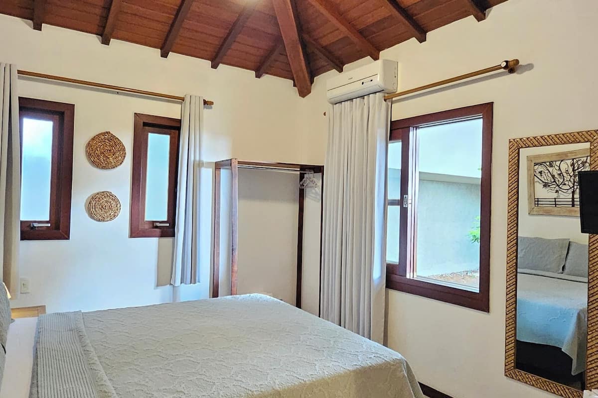 A bedroom with a bed, a ceiling fan, a window with curtains, a wall-mounted air conditioning unit, and a mirror.