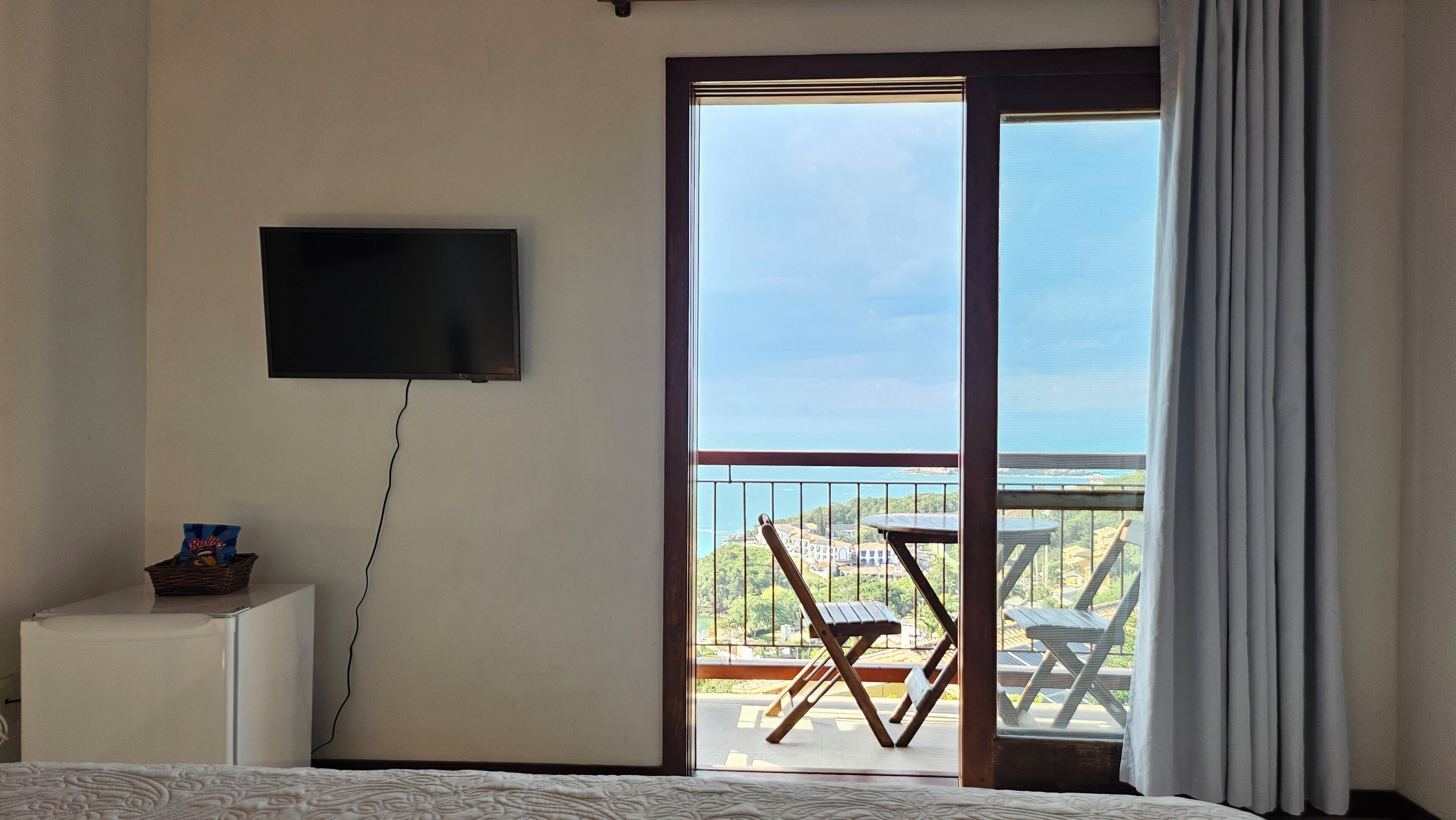 A bedroom with a TV, a small table, a chair, and a balcony with a view.