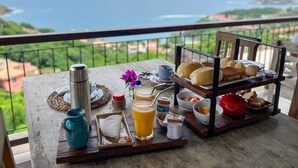 Bandeja de desayuno con pan, pasteles y fruta en un balcón con vistas panorámicas.
