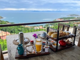 Bandeja de desayuno con pan, pasteles y fruta en un balcón con vistas panorámicas.
