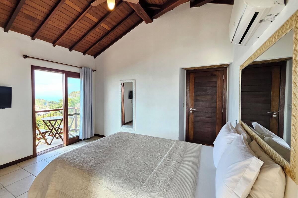 A bedroom with a bed, a TV, a balcony, and a door.