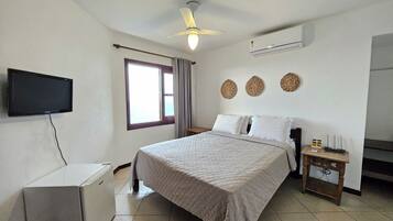 Un dormitorio con cama, televisión, aire acondicionado, ventilador de techo y ventana con cortinas.