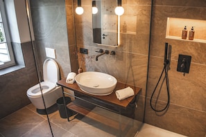 A modern bathroom with a glass-enclosed shower, a white sink, and a toilet. - Suiten Zantl (Bad Toelz)