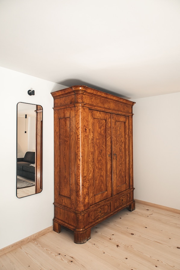 A wooden wardrobe in a room with a mirror on the wall and a light switch above it. - Suiten Zantl (Bad Toelz)