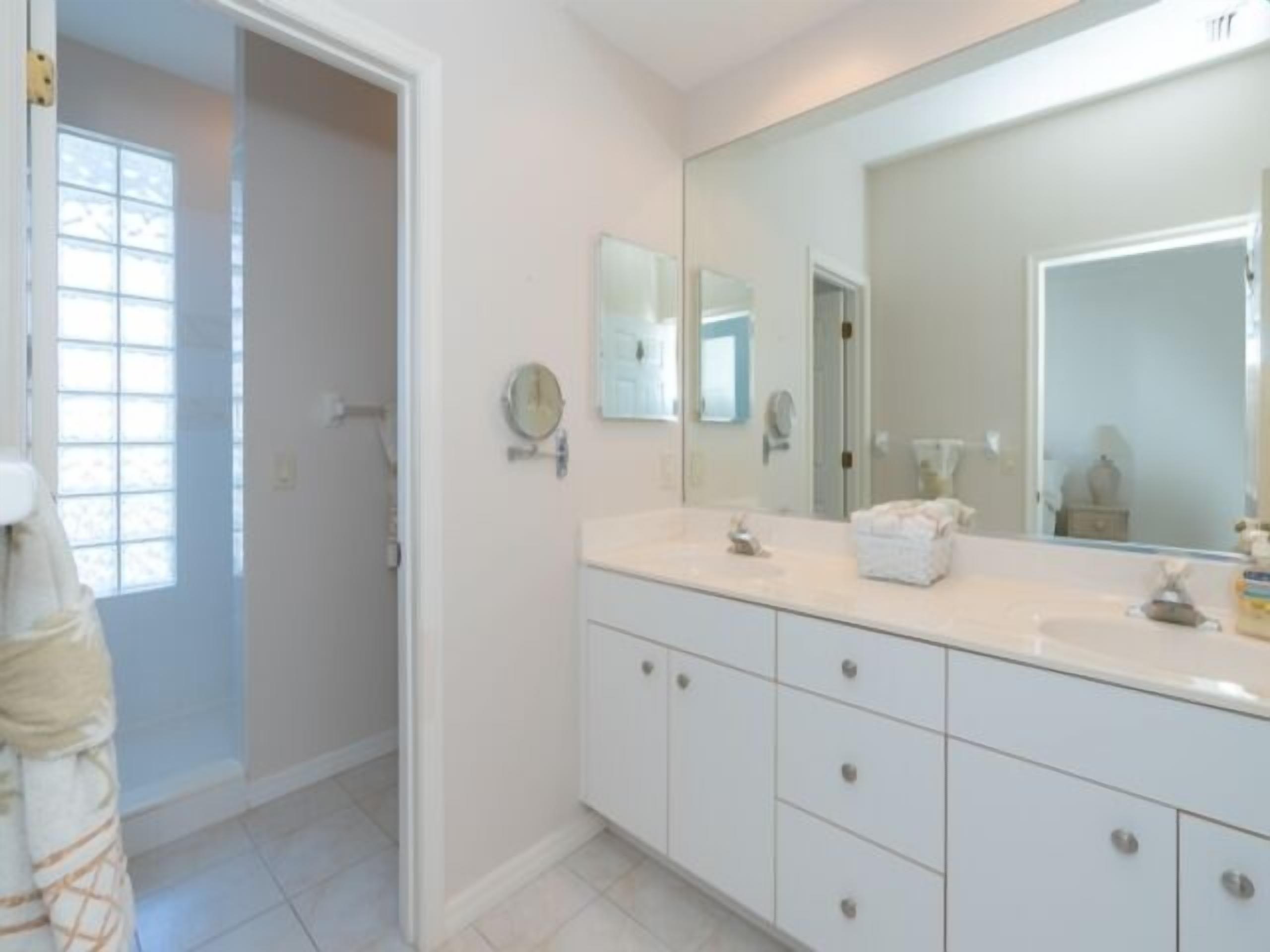 A bathroom with a large mirror, white cabinets, and a towel rack.