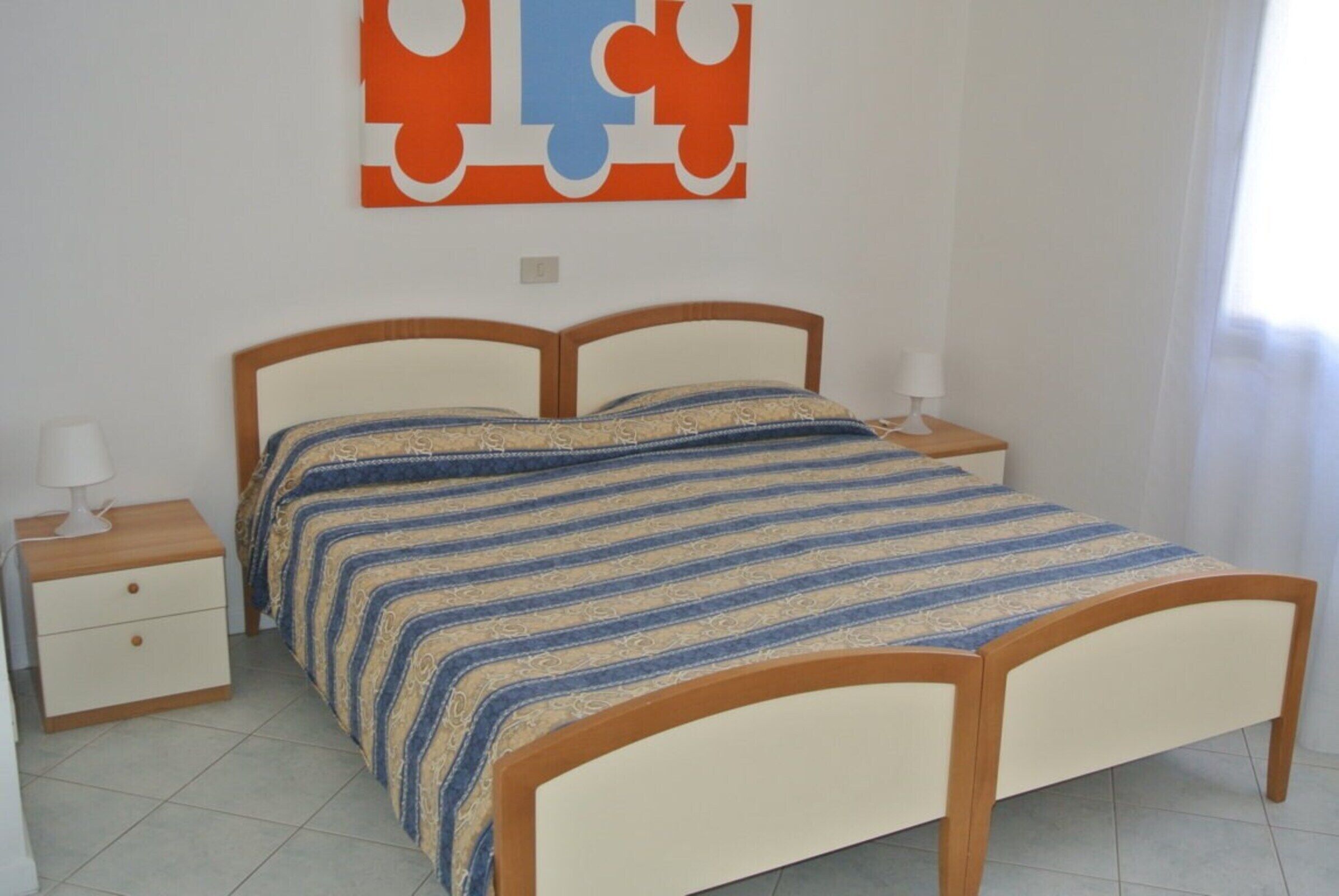 A bedroom with a bed, nightstands, a wall art piece, and a window.