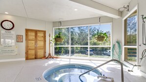 Een spa-ruimte met een whirlpool, houten deuren en een groot raam met planten.