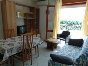 A living room with a sofa, chairs, a television, a dining table, and a balcony with a railing. - Cozy Apartment 150m From the sea (Lignano Sabbiadoro)
