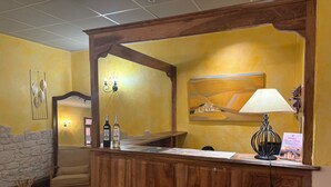 A reception desk with a wooden finish, a lamp, and two bottles of wine. - Hôtel de Provence (Digne-les-Bains)