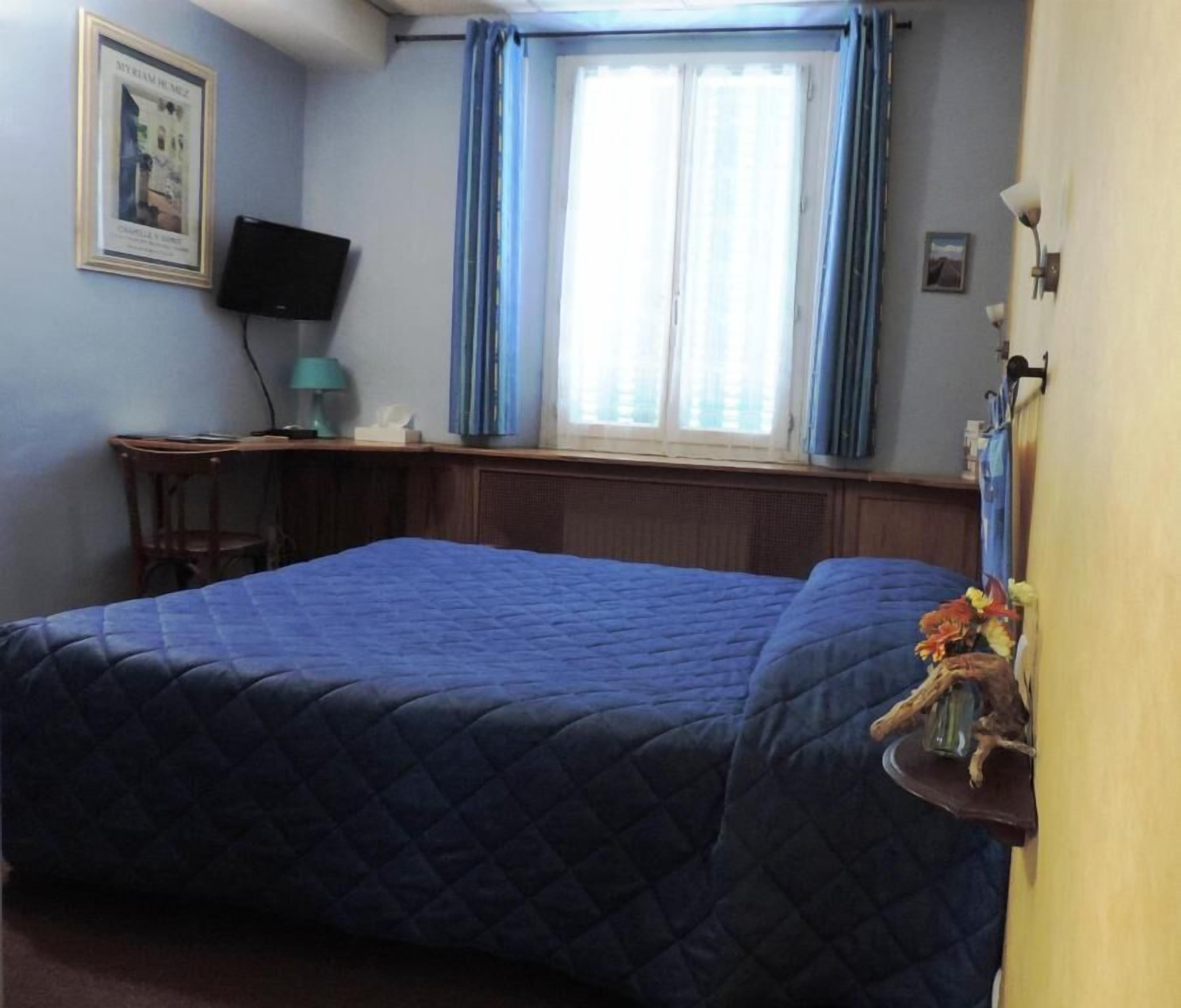 A bedroom with a large bed, a desk with a computer, and a window with curtains.