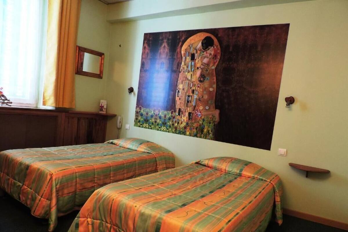 Une chambre d’hôtel avec deux lits, un grand tableau au mur, une fenêtre avec des rideaux et un petit bureau avec un téléphone.