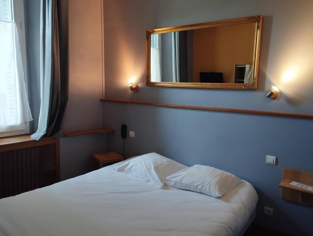 Une chambre d’hôtel avec un lit, un miroir, une table de chevet et une fenêtre avec des rideaux.