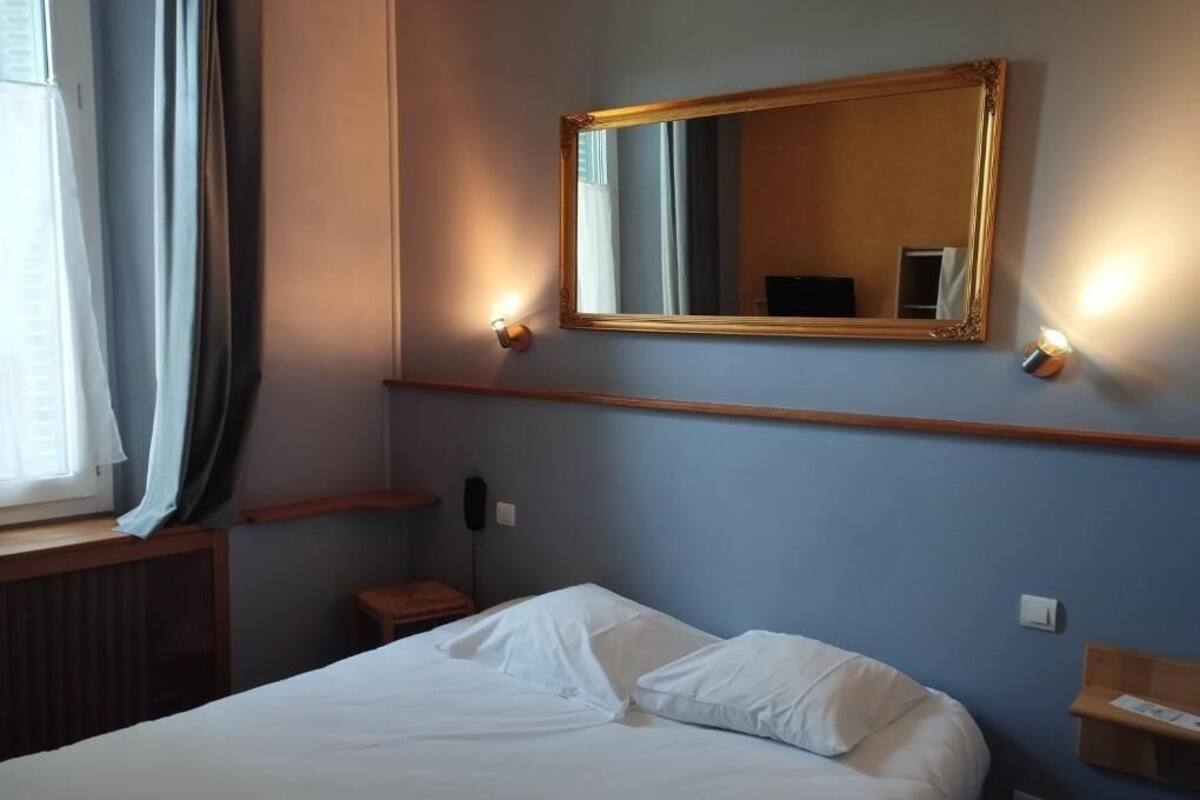 Une chambre d’hôtel avec un lit, un miroir, une table de chevet et une fenêtre avec des rideaux.