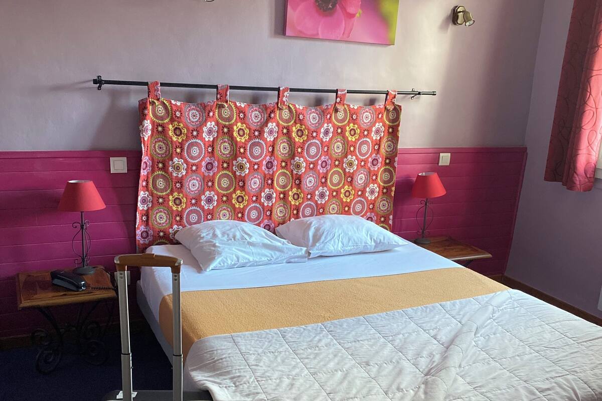 Une chambre d’hôtel avec un lit, une valise, une table avec une lampe et un tableau au mur.