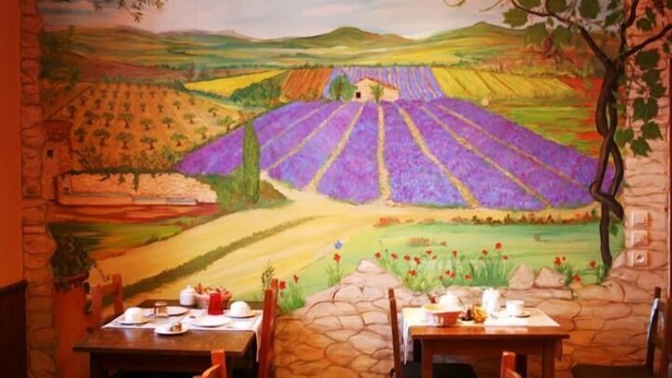 A dining area with a mural of a vineyard landscape, stone tables, and chairs. - Hôtel de Provence (Digne-les-Bains)
