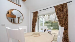Een ronde tafel met een witte stoel, een ronde spiegel aan de muur, en een uitzicht op een tuin door een raam met gordijnen.