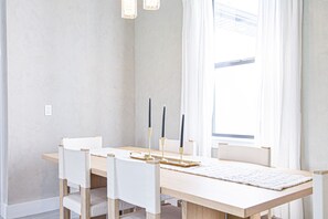 Een eetruimte met een houten tafel, witte stoelen en een kandelaar met kaarsen.