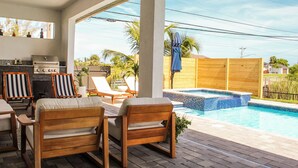 Eine Terrasse mit Pool, Holzmöbeln und Grill.