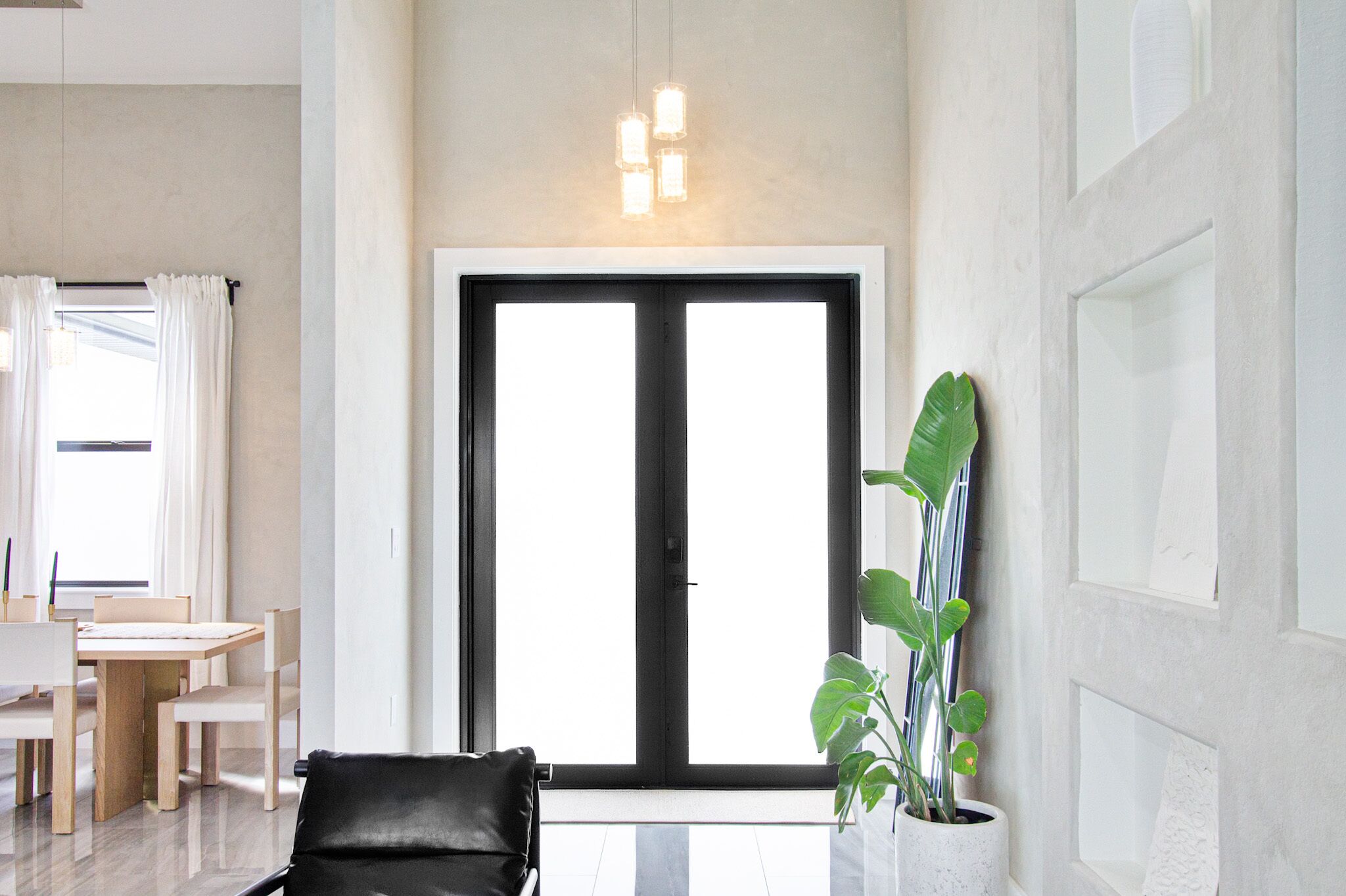 Una sala de estar moderna con un amplio ventanal corredera, una zona de comedor con mesa y sillas de madera, y una planta en maceta.