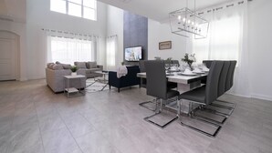 A modern living room with a dining area, featuring a large TV, grey sofas, and a chandelier. - 1153 KS -Luxury Oasis 5BR/5BA Home, Private Pool (Four Corners)