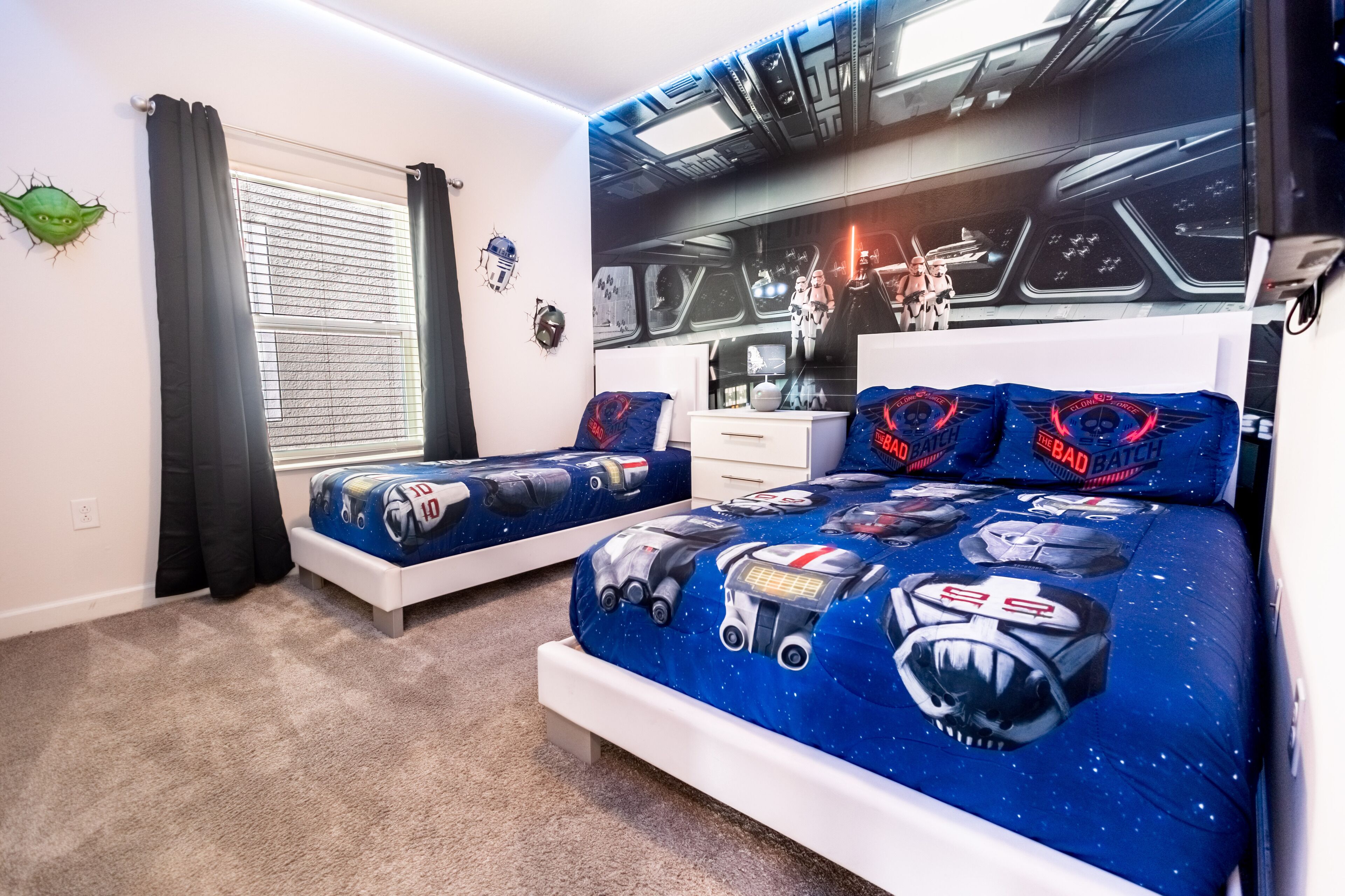 Een slaapkamer met twee bedden, Star Wars beddengoed, een raam met gordijnen, en Star Wars beeldjes aan de muur.