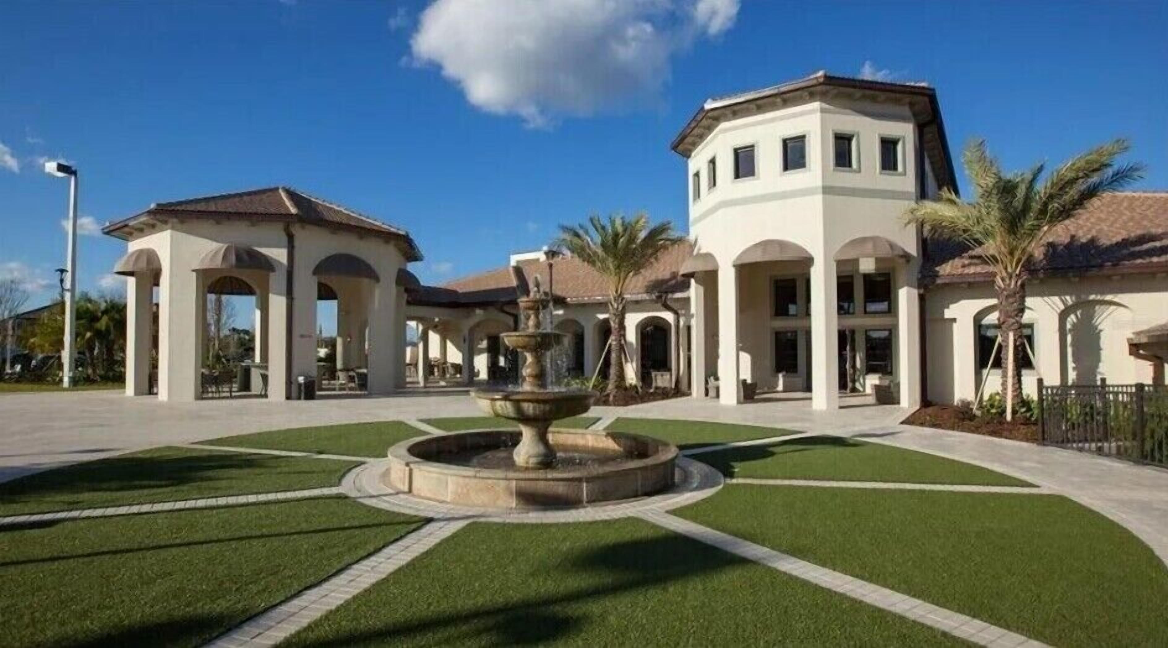 A building with a central fountain, surrounded by a well-maintained lawn and palm trees.
