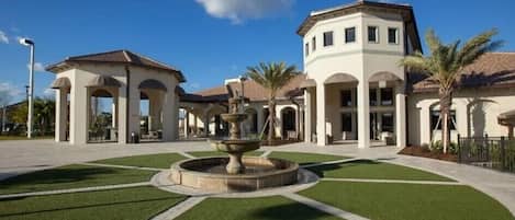 A building with a central fountain, surrounded by a well-maintained lawn and palm trees.
